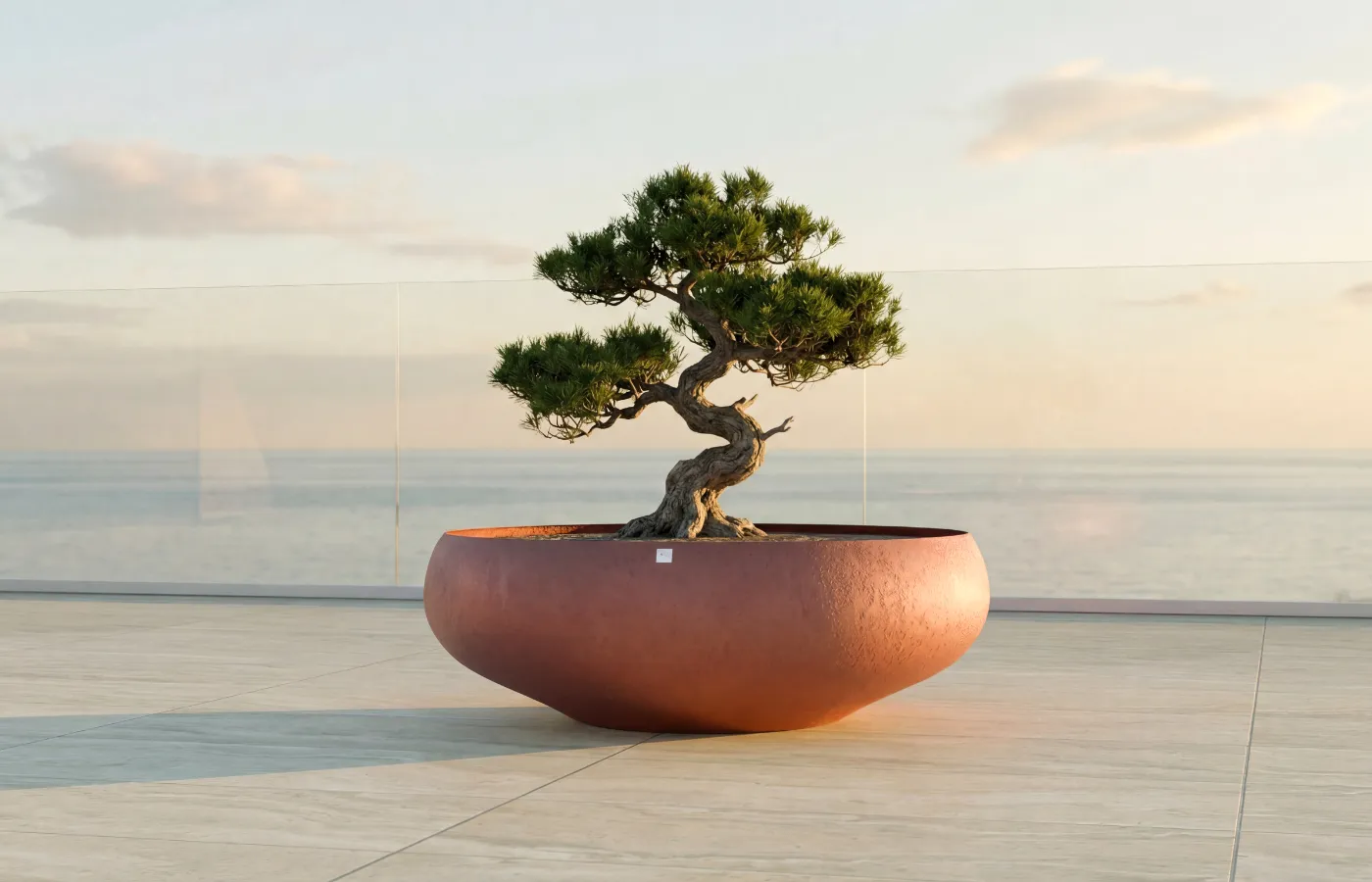 Floreira Ariel em terraço com vista mar, com corpo arredondado baixo em vermelho e bonsai moldado ao centro.