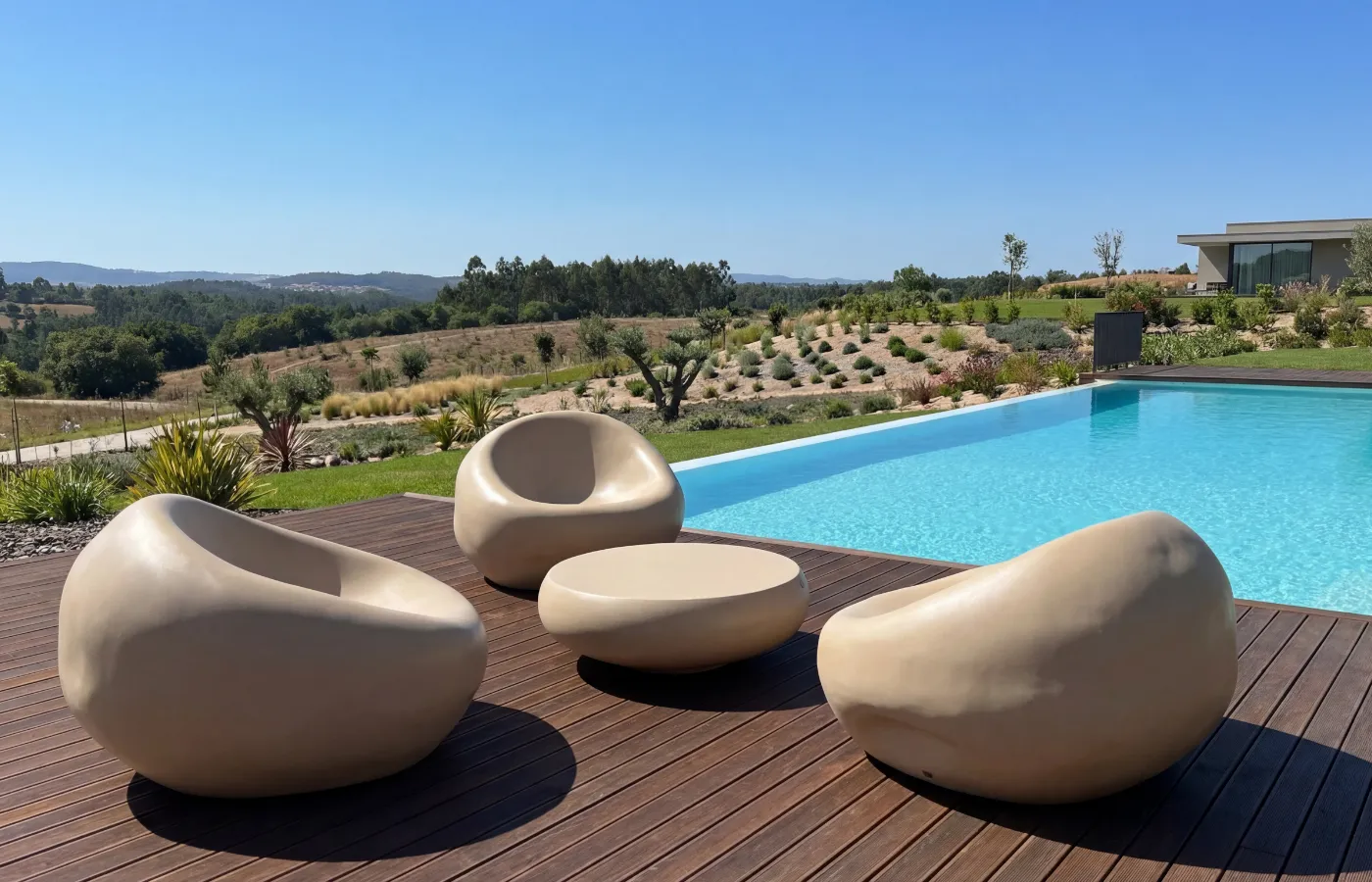 Mesa de centro Ariel de exterior em acabamento bege, integrada num conjunto de sofás Cobble junto a piscina sobre deck de madeira.