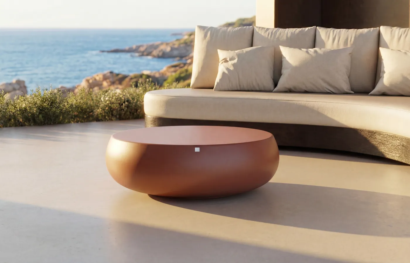 Mesa de centro Ariel de exterior em acabamento terracota, colocada diante de um sofá Harmony em ambiente junto ao mar.