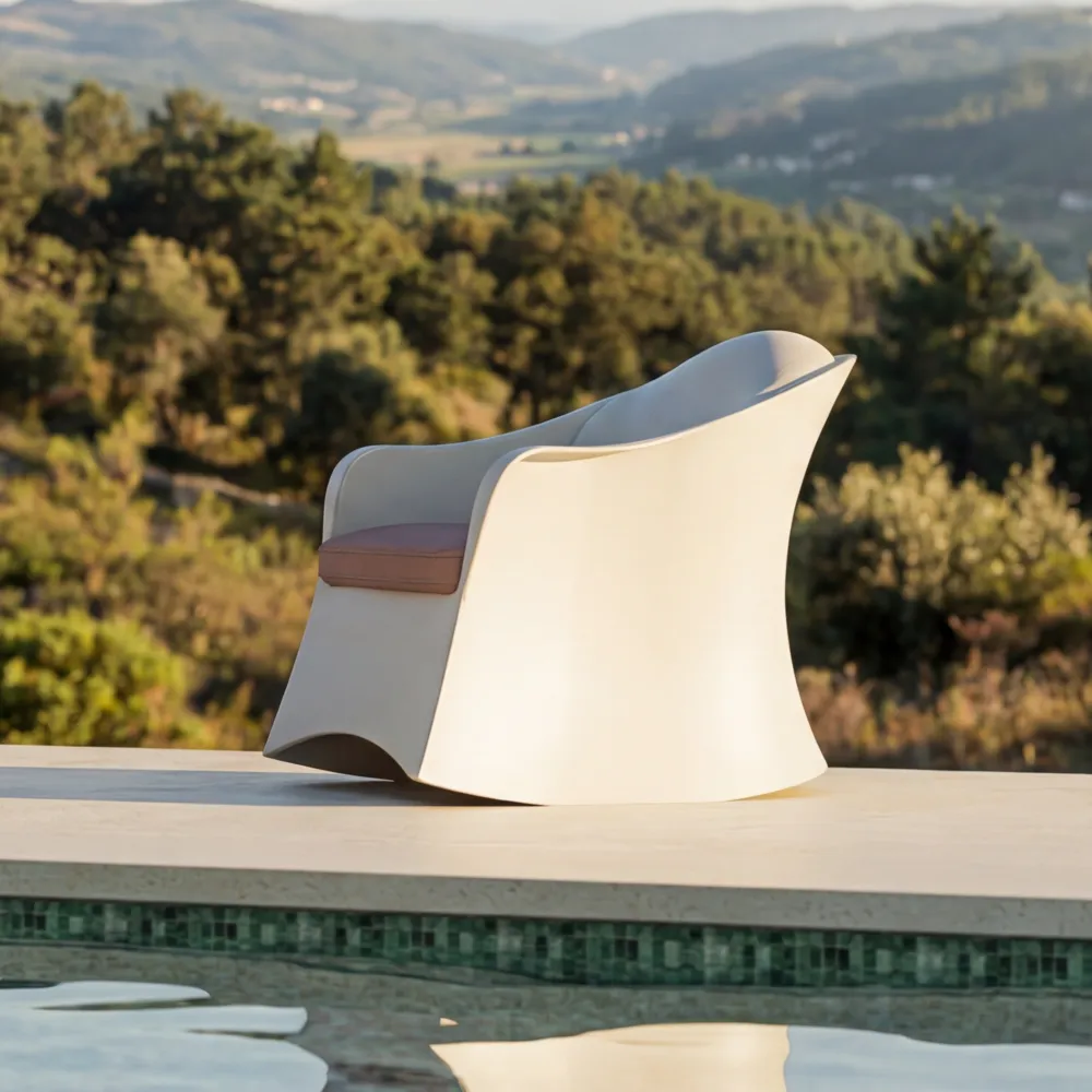 Vista lateral do cadeirão Brisa em branco, com encosto envolvente, curvatura contínua e almofada de assento em ambiente exterior.