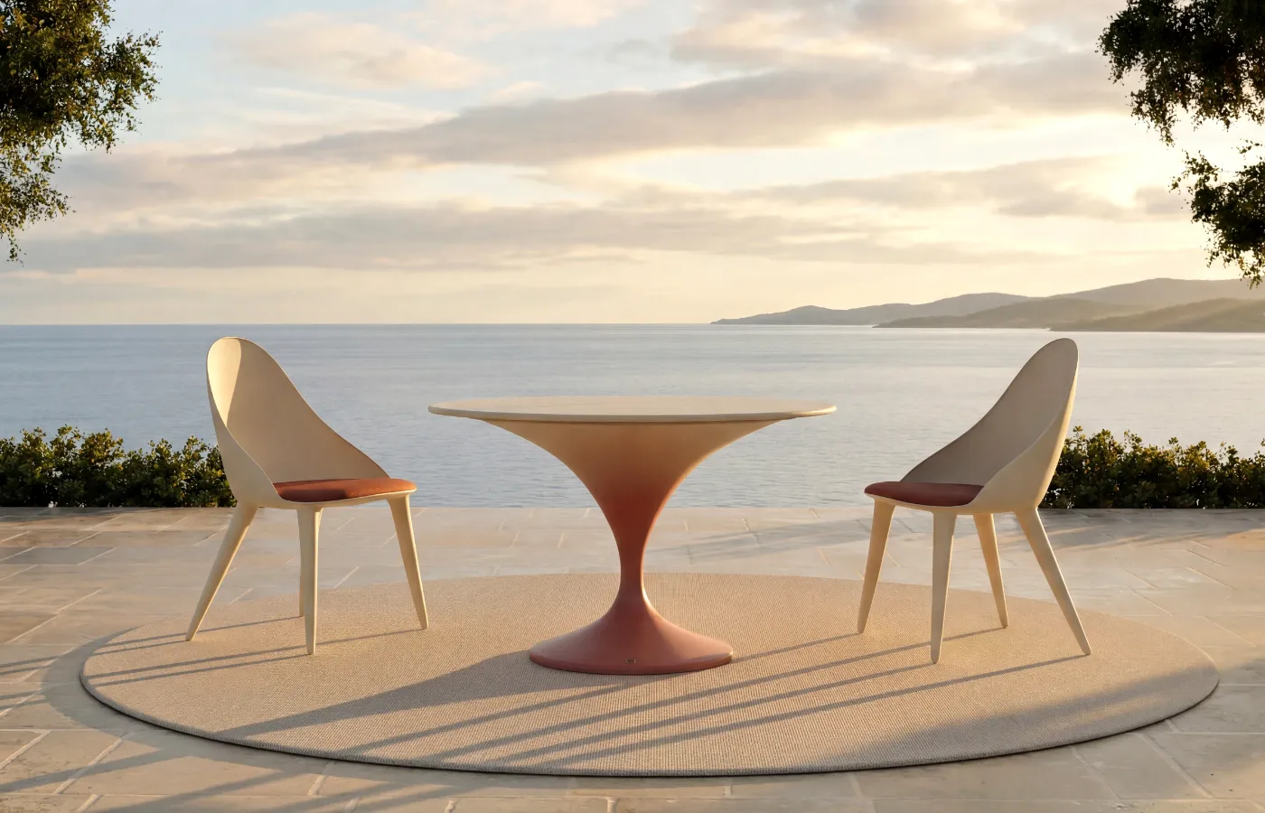 Charm dining table with a white and terracotta gradient finish on a seaside terrace, with a round top and curved central base between two Mónaco chairs.
