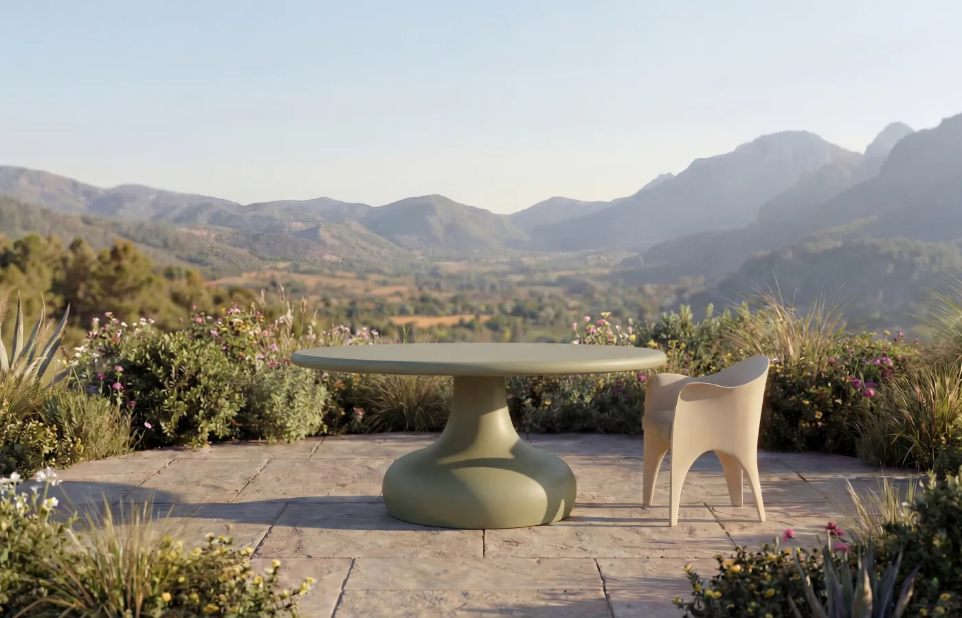 A light green Dora dining table on a landscaped terrace, with a round top and rounded central base, paired with one chair.