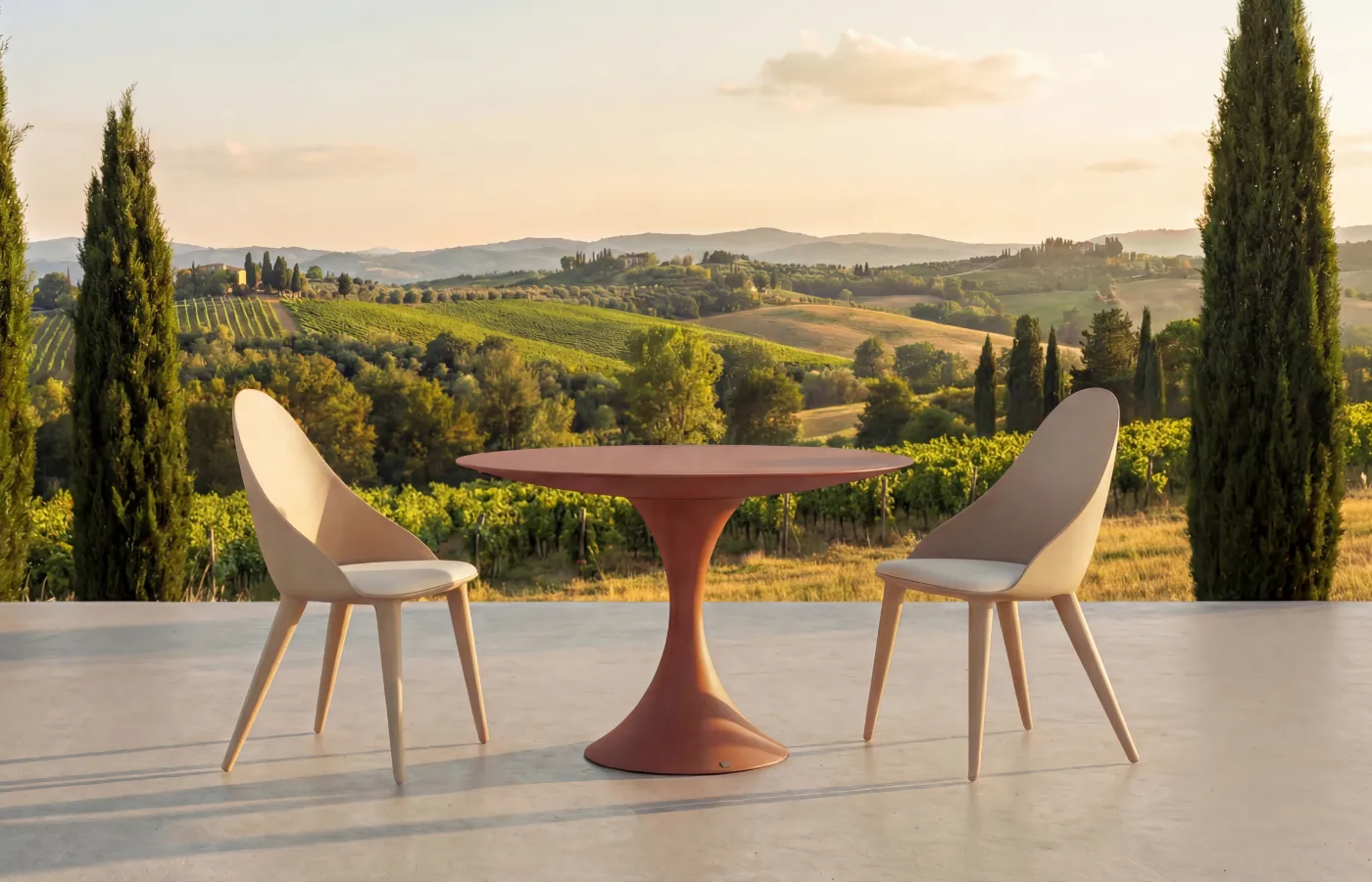 Mesa de jantar redonda Jade em terracota para exterior, entre duas cadeiras Mónaco, numa varanda com vista sobre vinhas e colinas.