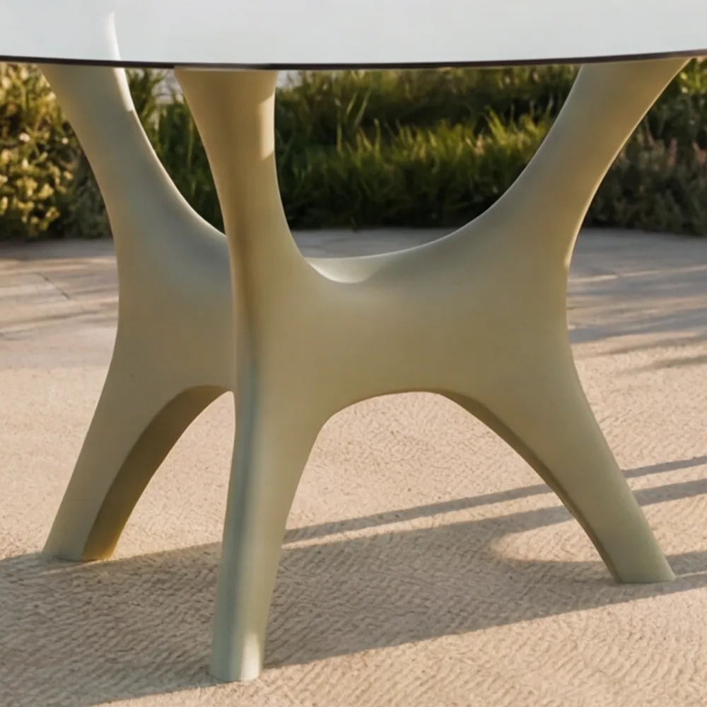 Detalhe da mesa de jantar Kosmos para exterior em verde suave, com base de três apoios curvos sob tampo redondo em vidro.