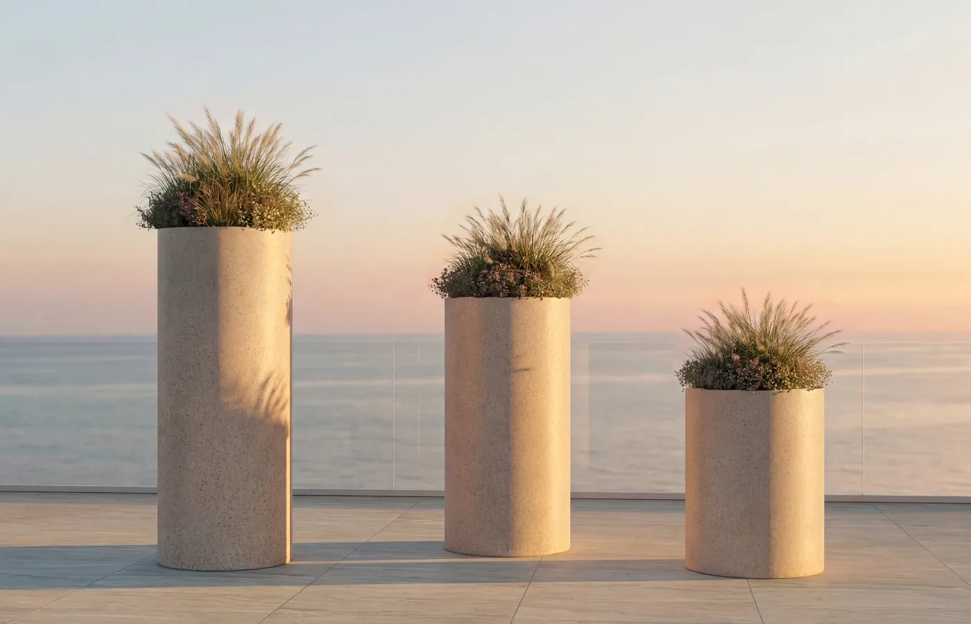 Vasos Magnus brancos em diferentes alturas num terraço com vista mar, com formas cilíndricas e composição leve de folhagens.