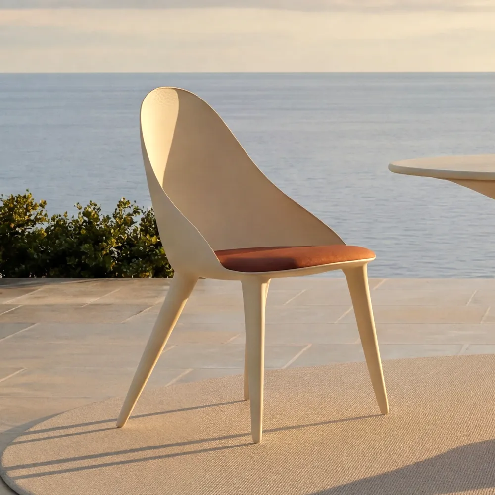 Detail of the Mónaco chair in white in profile, with a continuous curved backrest, cushioned seat and tapered legs in an outdoor setting
