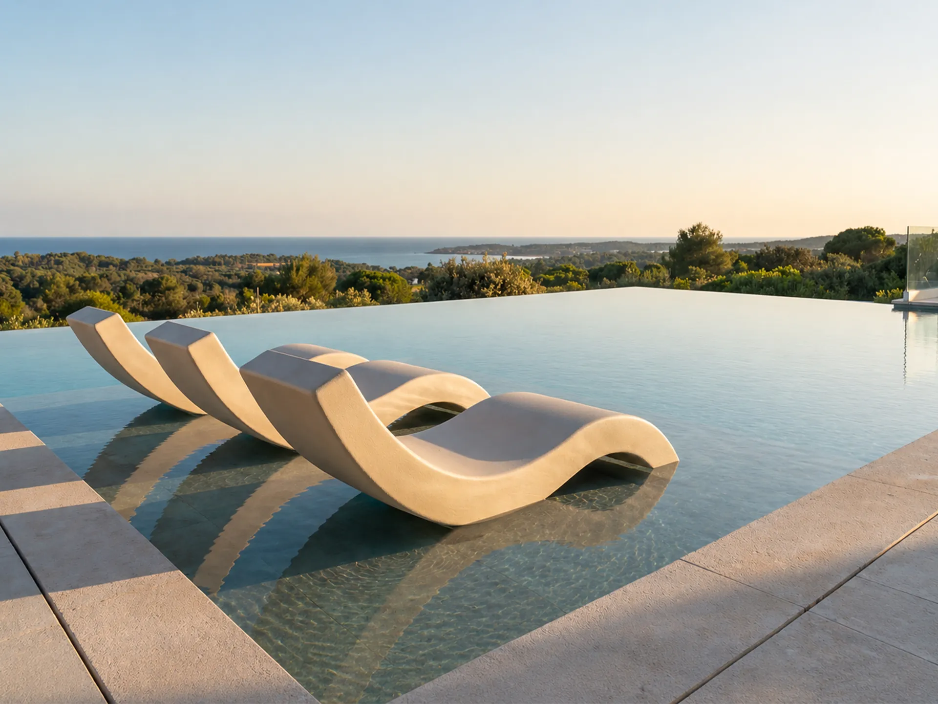 Chaise longues Nordic em bege alinhadas em zona pouco funda da piscina, com perfil curvo contínuo e vista mar ao fundo.