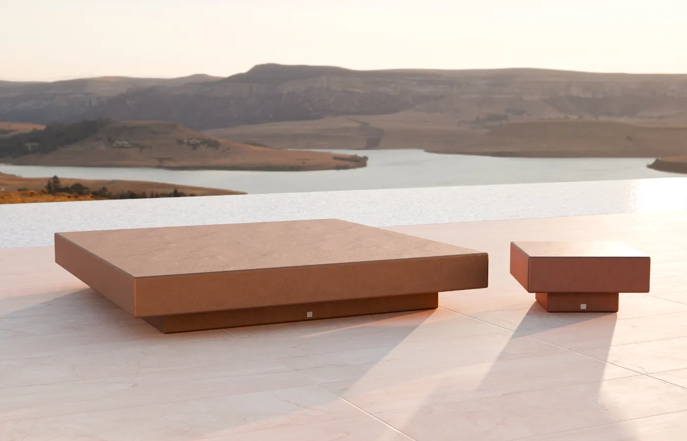 Conjunto de mesas de centro e apoio Nordic para exterior em acabamento terracota, colocado em terraço com vista para o lago.
