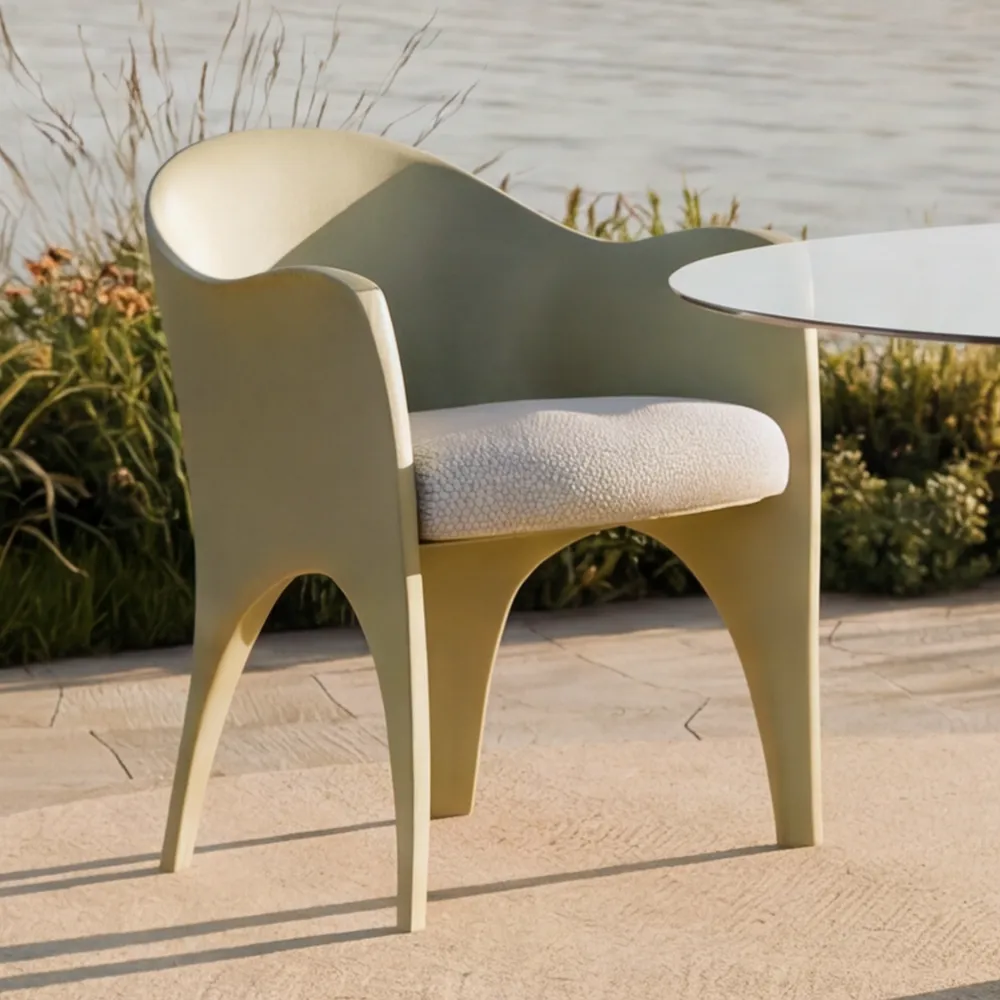 Detail of the Oceano chair in light green with a continuous backrest, integrated arms and a cushioned seat beside an outdoor table.