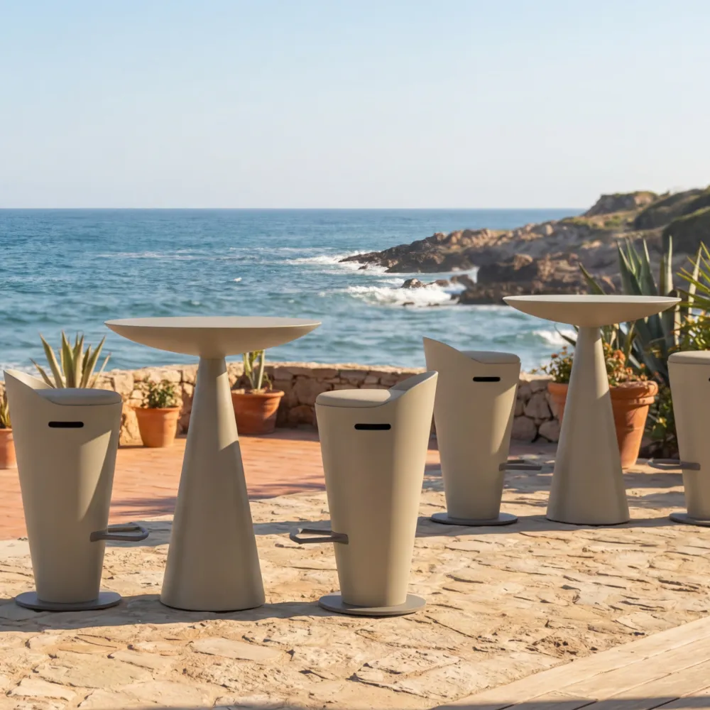 Oceano bar table set and beige stools in a beach setting with a view of the sea.