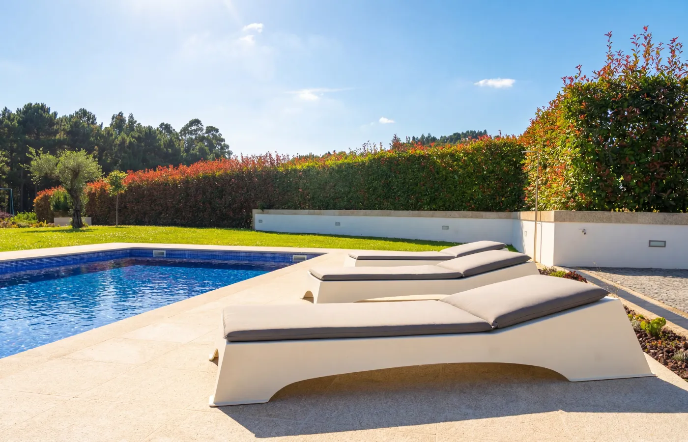 Quadra chaise longues by the pool, with a white straight base, arched cut-out and continuous cushions in an outdoor setting.