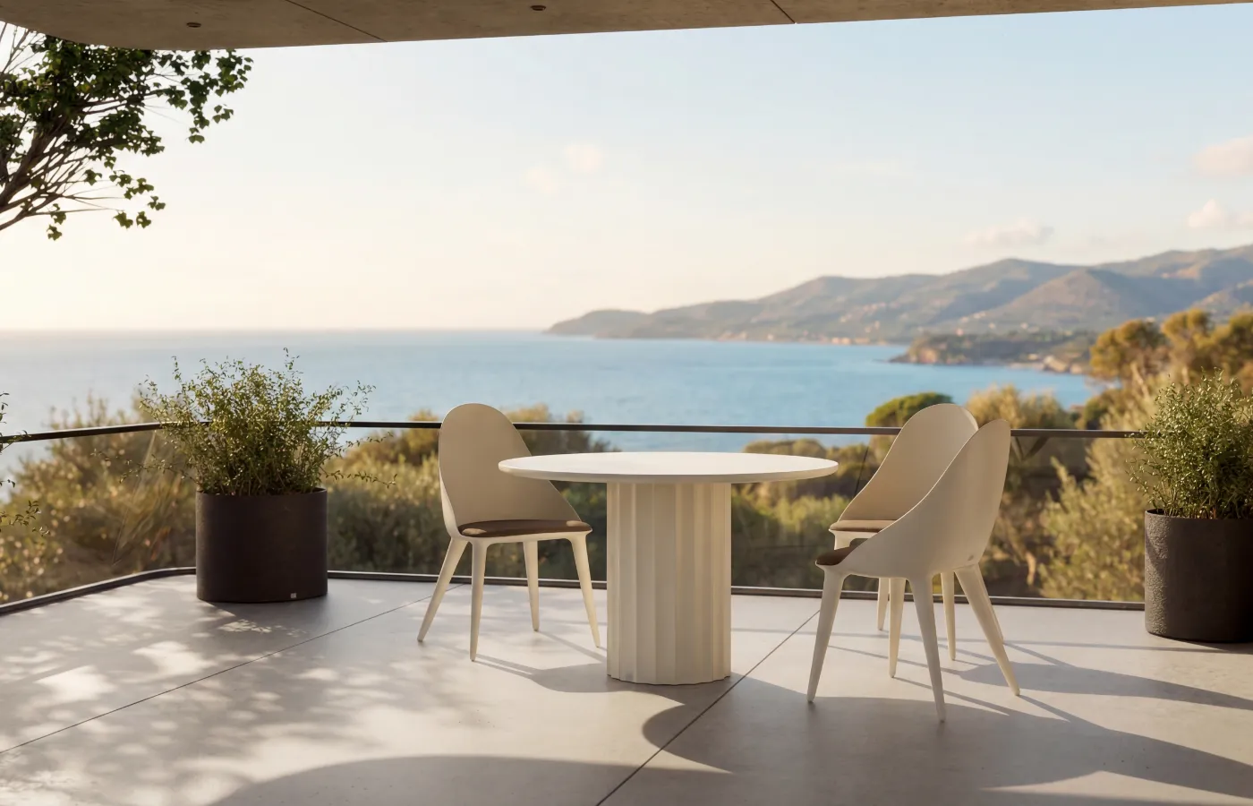 Roma round outdoor dining table in matte white, with a fluted base, surrounded by three Mónaco chairs on a sea-view terrace.
