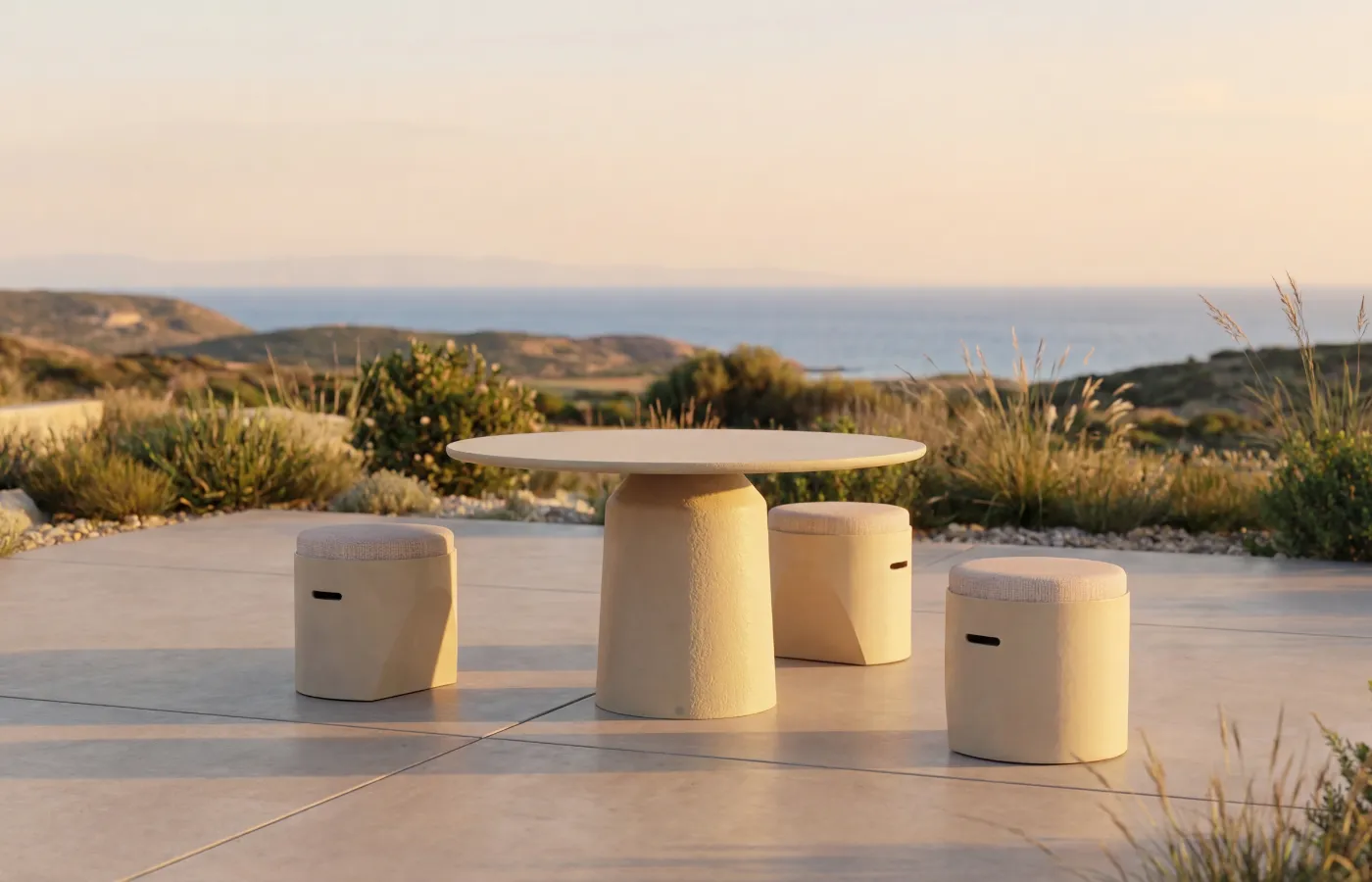 Siana round outdoor dining table in beige, with a textured cylindrical base, surrounded by three Cloe Stools with a sea view.