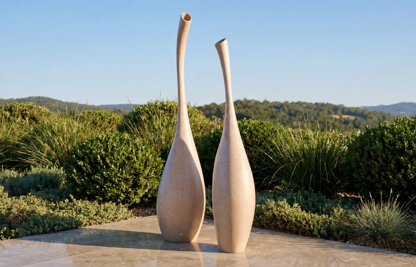 Solitary decorative pieces in an outdoor garden, with tall, elongated organic shapes in sand finish on a stone floor.